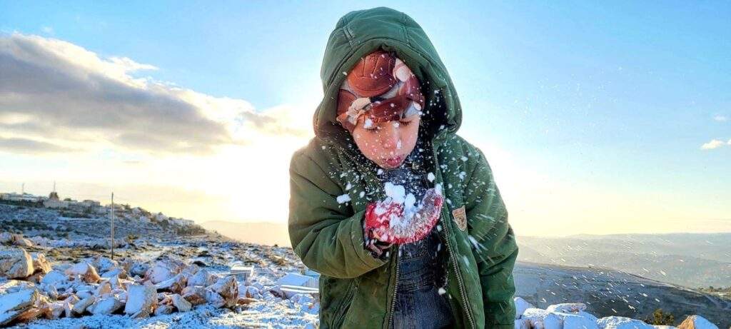 a young boy blows a handful snow as the sun rises in Israel
